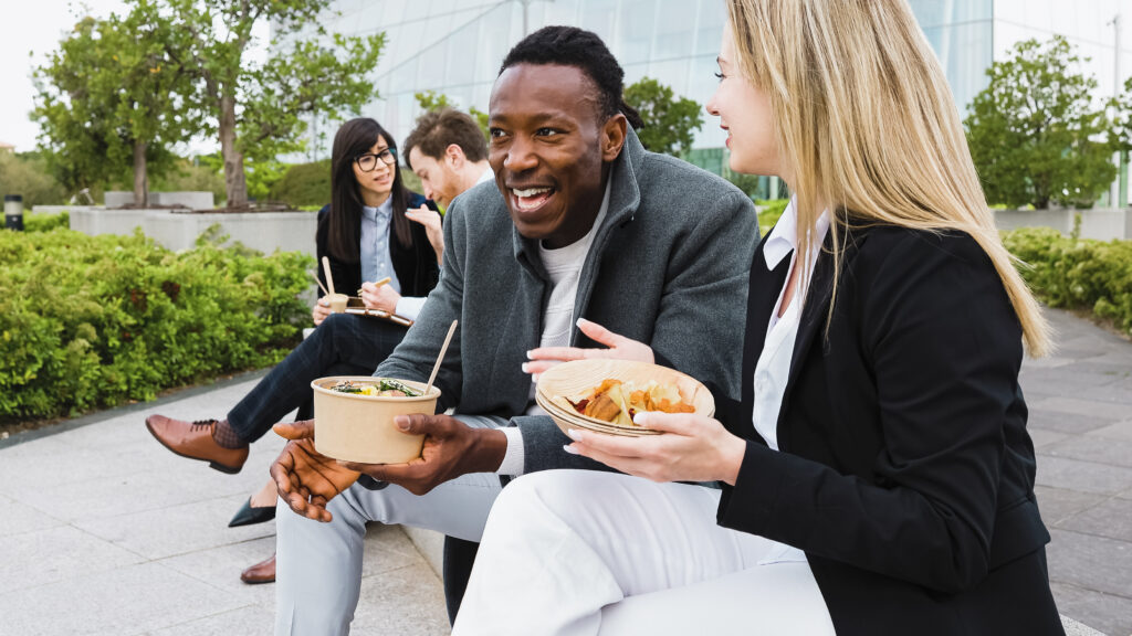 Employees enjoying a healthy lunch break together outdoors as part of a workplace wellness culture that supports wellbeing and social connection.